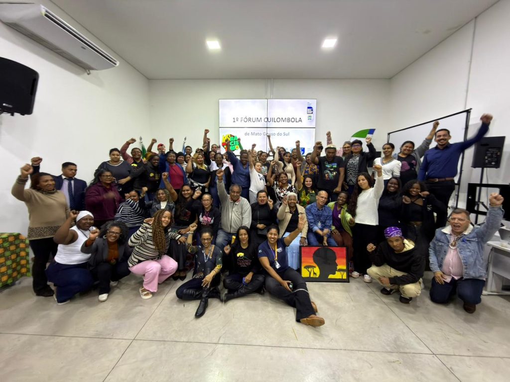 Foto em grupo de dezenas de participantes do "1º Fórum Quilombola de Mato Grosso do Sul", muitos com os punhos erguidos em sinal de resistência e celebração.
